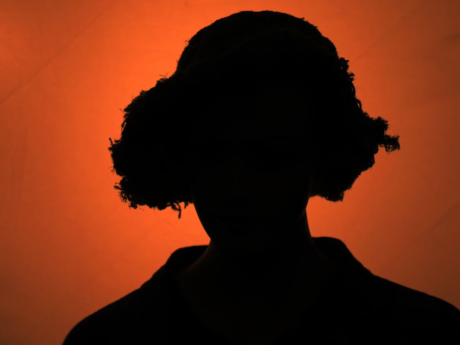 Dramatic silhouette of a person with curly hair against a vibrant orange background.