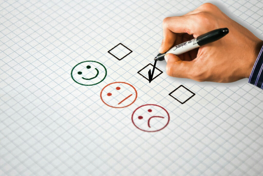Hand drawing a check mark next to customer feedback icons showing happy, neutral, and unhappy faces.