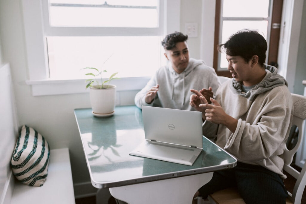 Two people discussing work at a table with an open laptop in front of them.