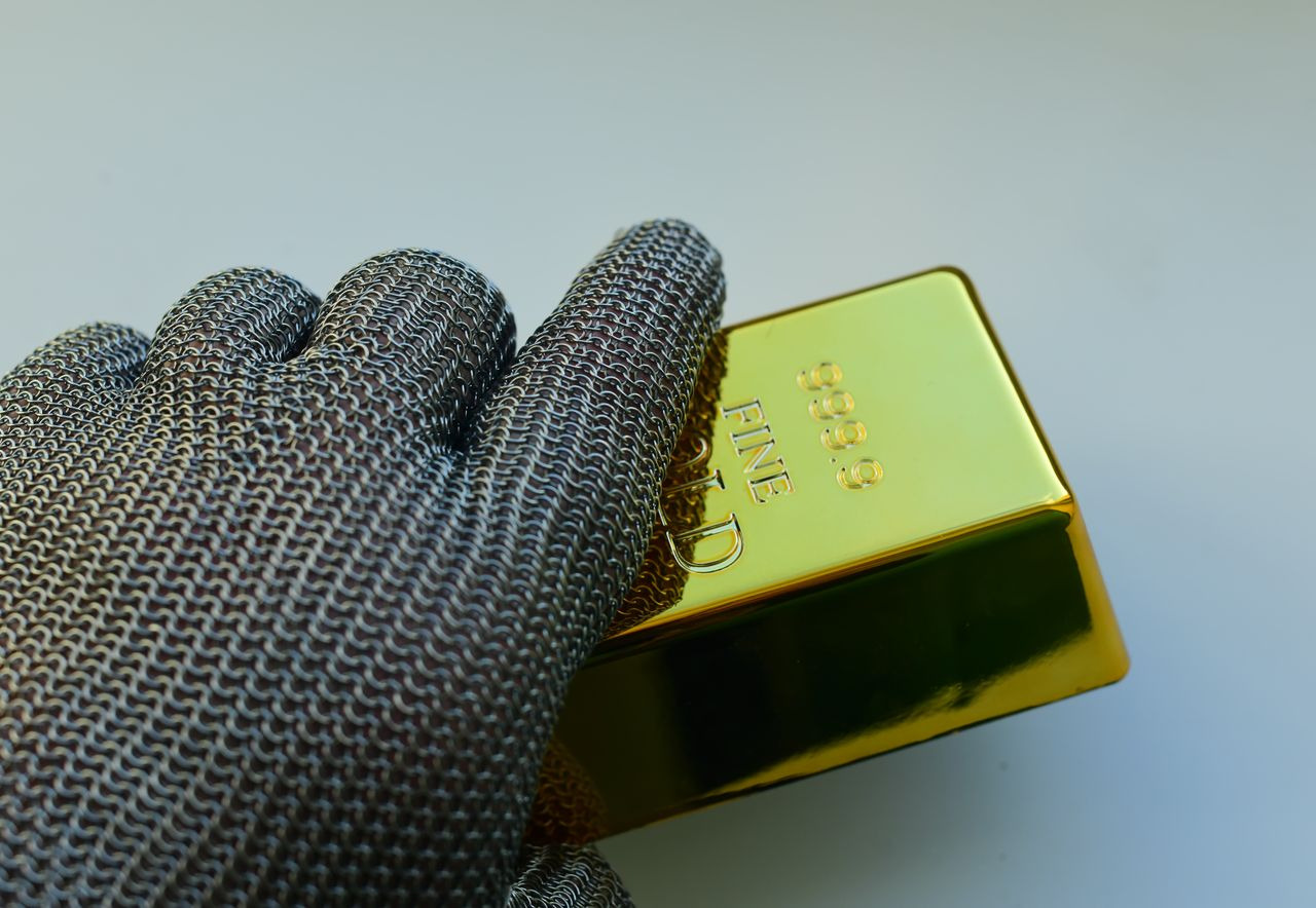 Gloved hand holding a gold bar