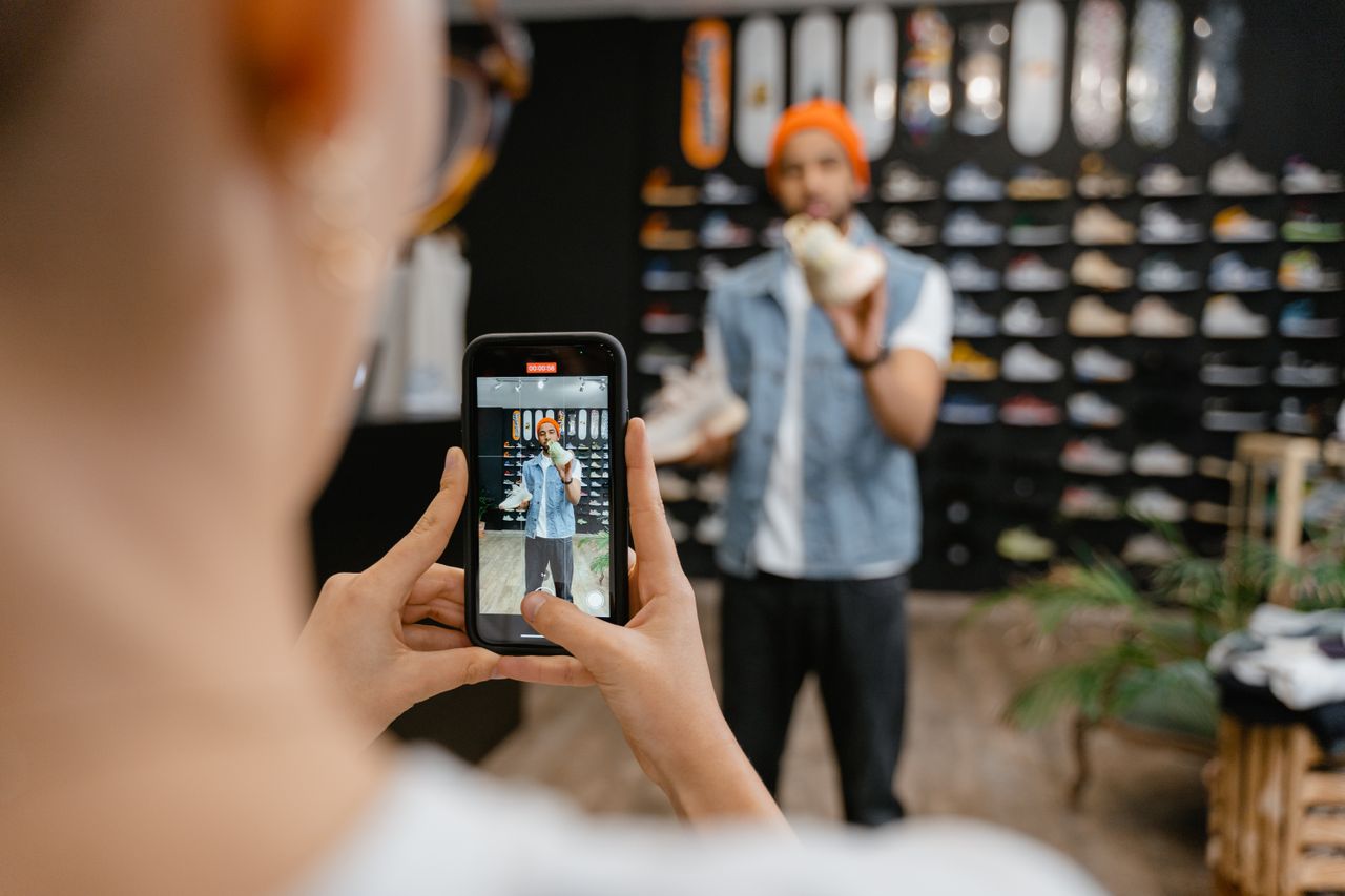 Person filming a man holding a sneaker inside a shoe store with a smartphone