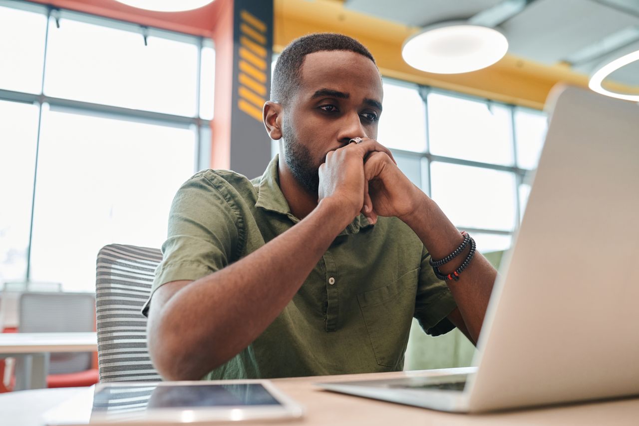 Man sitting at a desk with his hands clasped while looking at a laptop