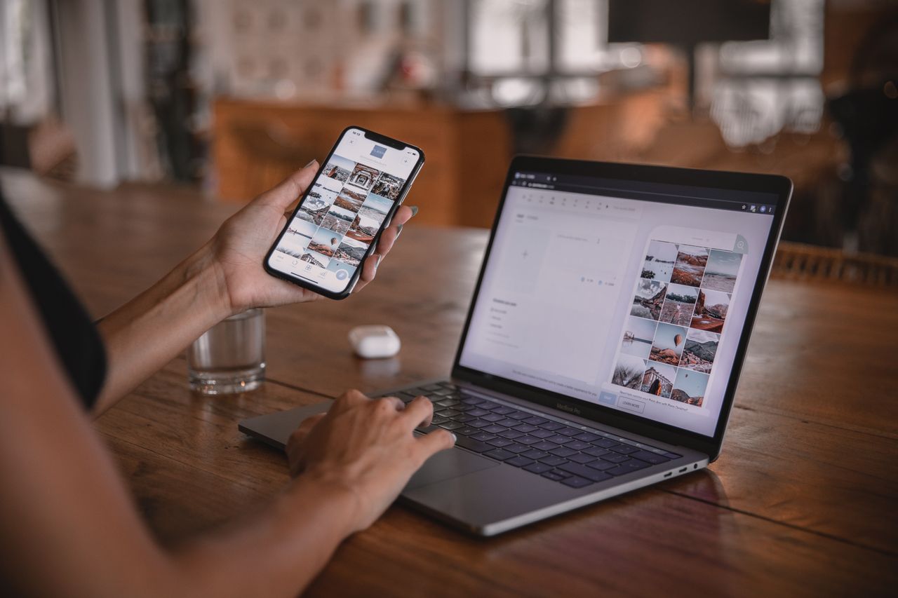 Person holding a smartphone while reviewing a grid of photos on a laptop