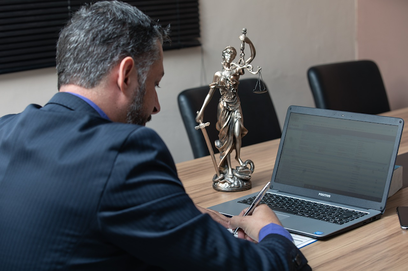 Lawyer writing beside a laptop and Lady Justice statue in a conference room