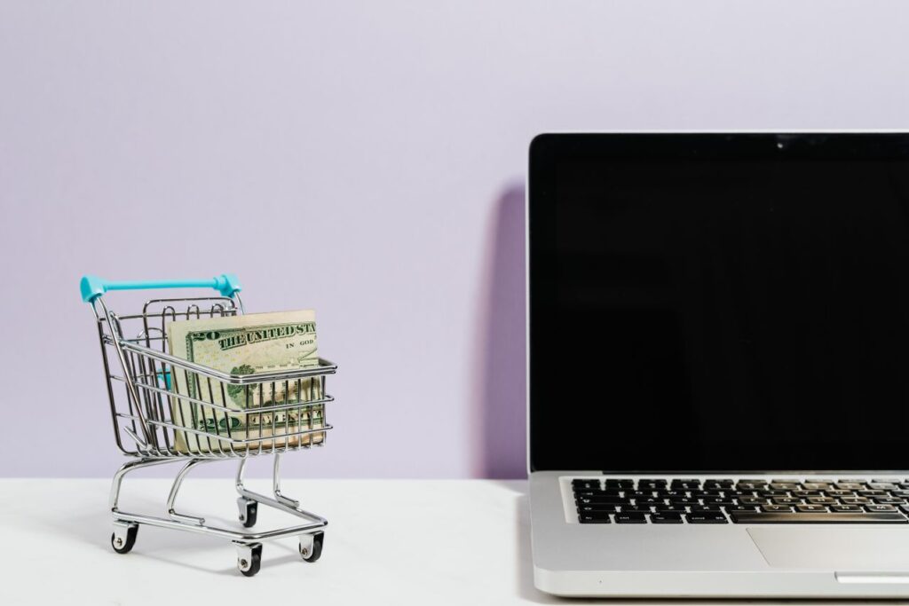 Miniature shopping cart holding cash beside an open laptop