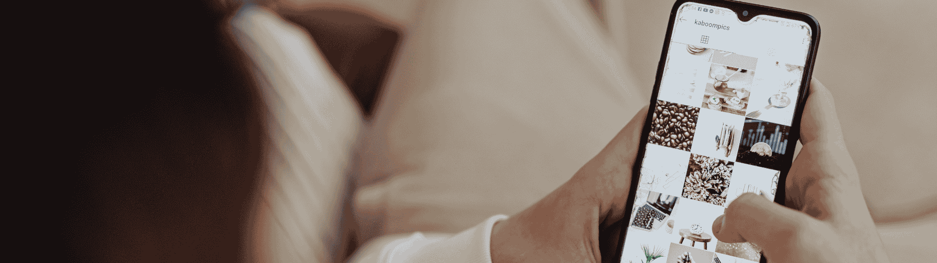 Person holding a smartphone and browsing an Instagram-style photo grid while sitting indoors in a relaxed setting.