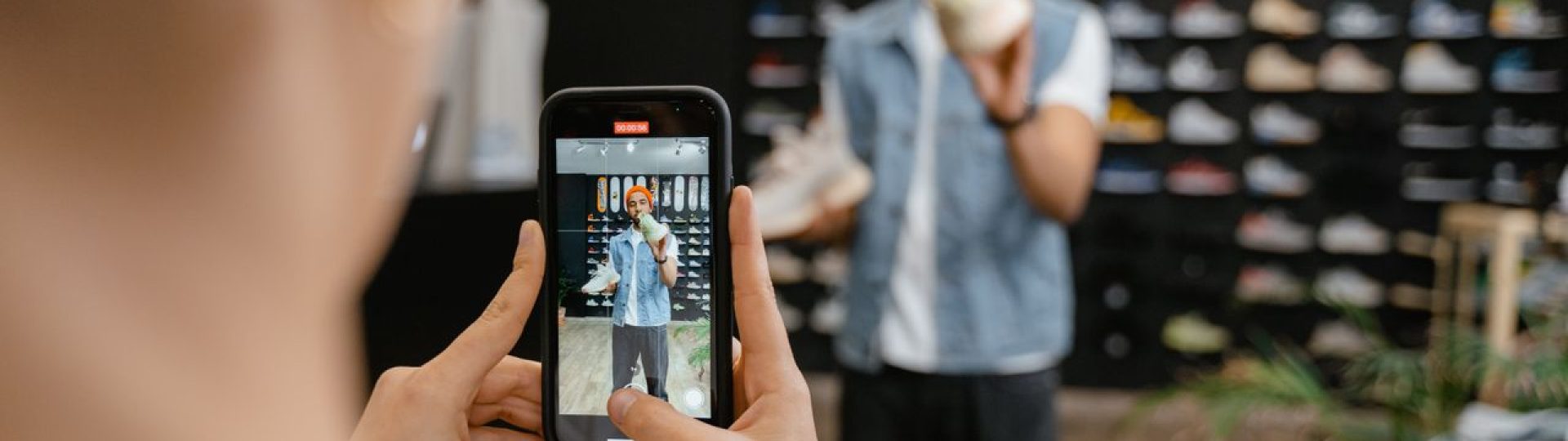 Person filming a man holding a sneaker inside a shoe store with a smartphone