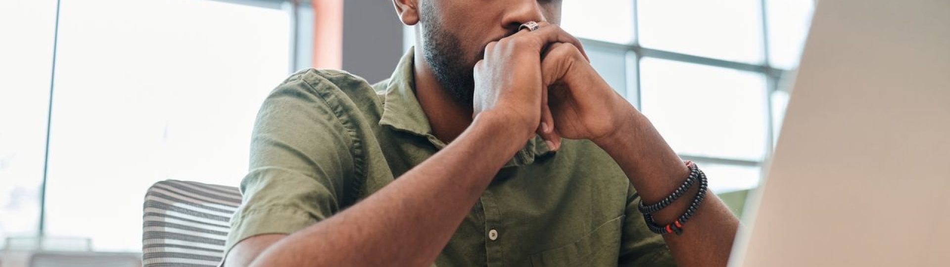 Man sitting at a desk with his hands clasped while looking at a laptop