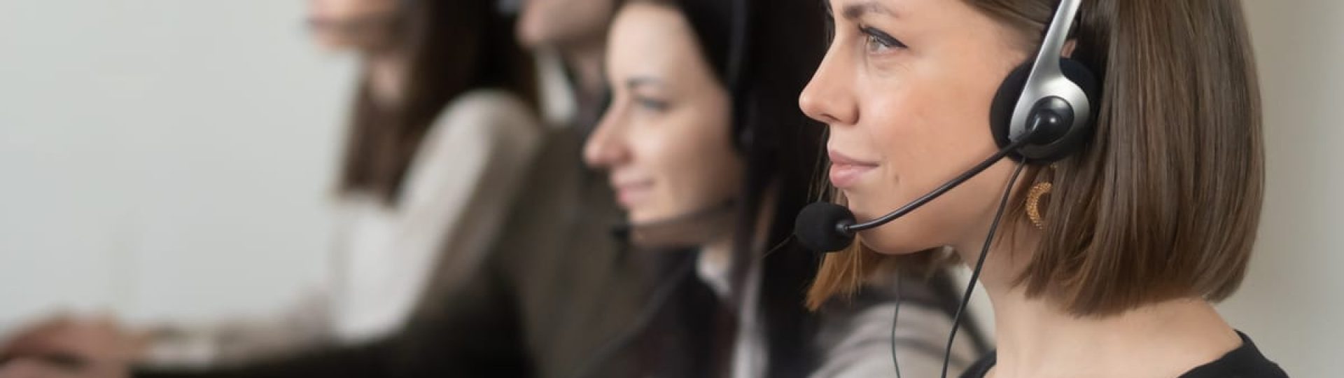 Side view of young coworkers in casual clothes sitting in light workplace with headphones with microphone while surfing on laptop