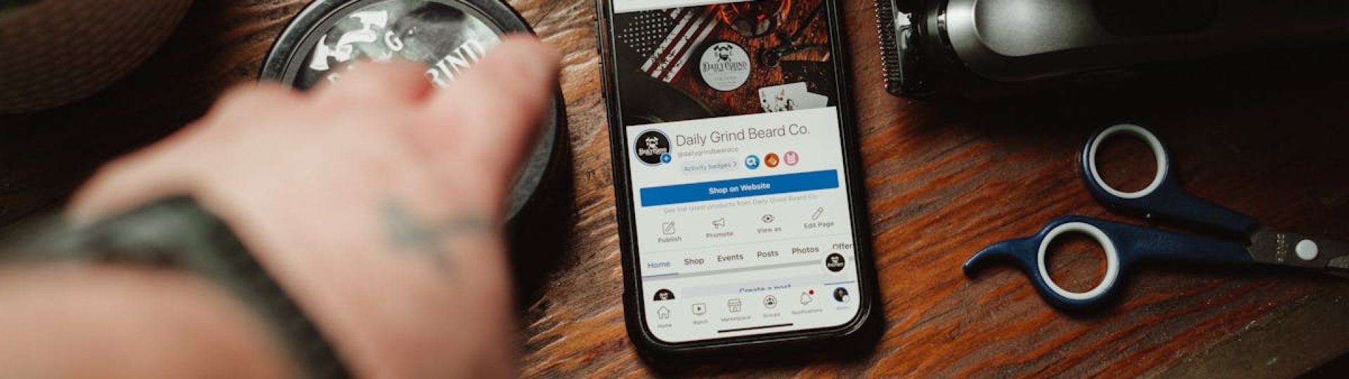 Barber tools and a smartphone showing a grooming brand site on a wooden table.