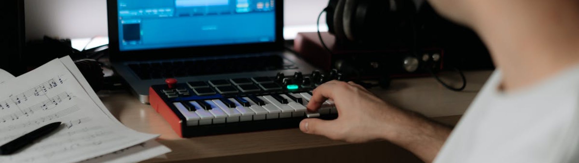 A music producer uses a synthesizer and laptop for composing in a home studio.