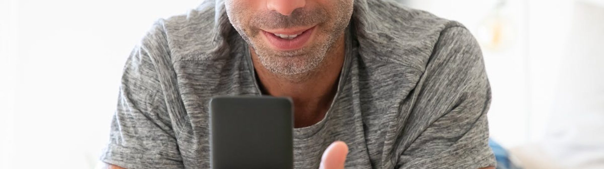 Adult man using smartphone comfortably indoors, conveying modern lifestyle.