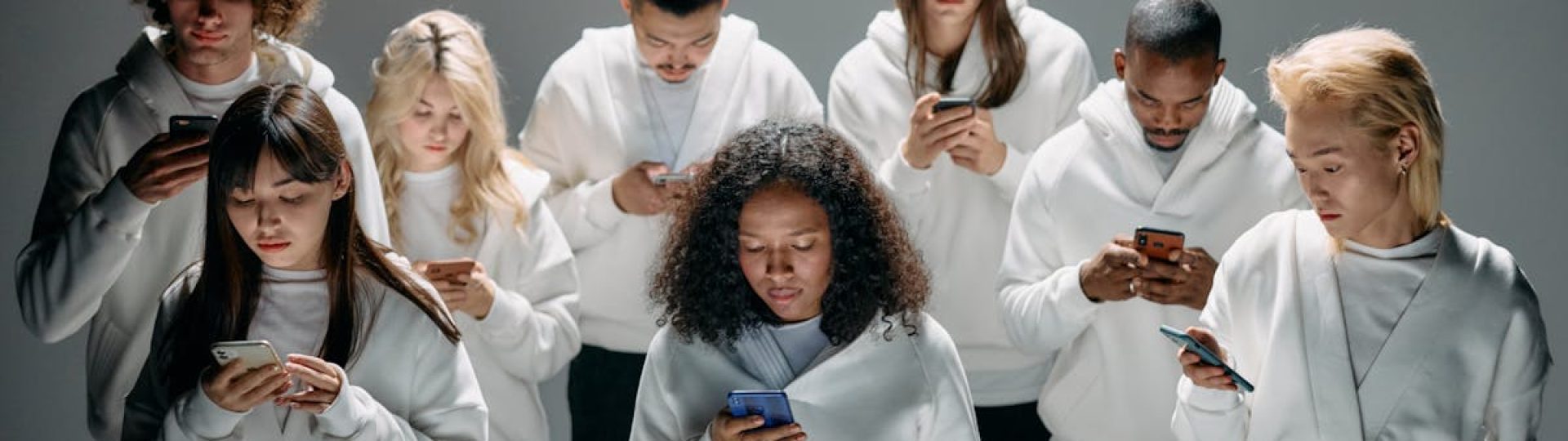 A diverse group of people in white hoodies engaged with smartphones, symbolizing social connection and isolation.