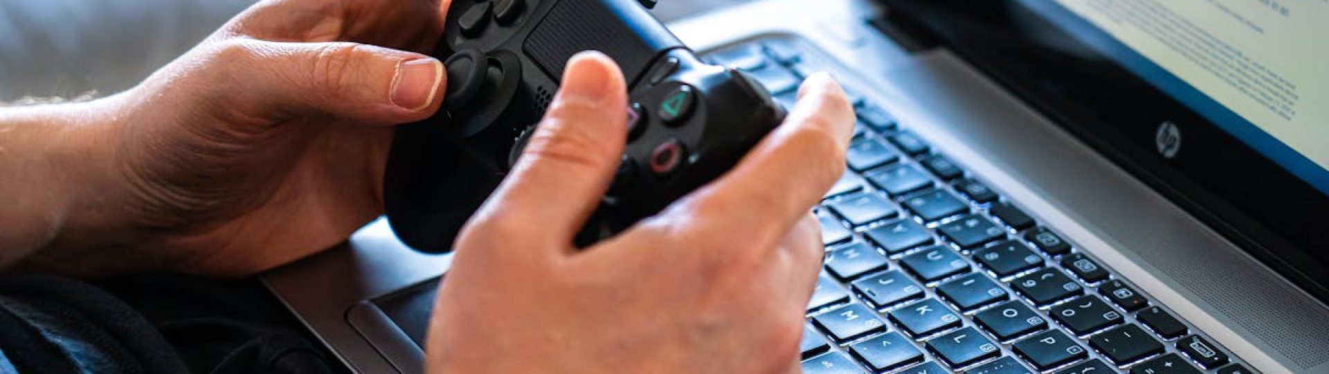 Person holds a gaming controller while interacting with a laptop, emphasizing modern gaming technology.