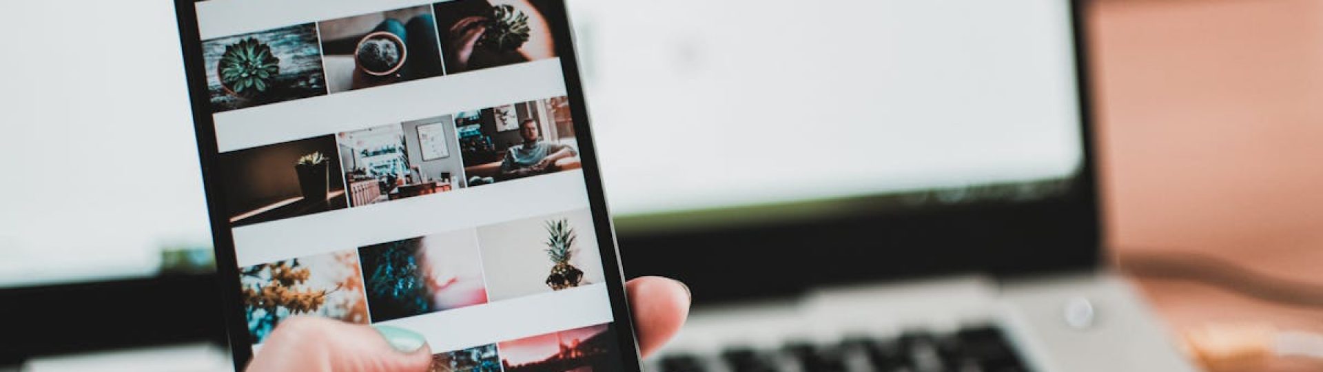 A person uses a smartphone to browse social media in front of a laptop, emphasizing modern technology and lifestyle.