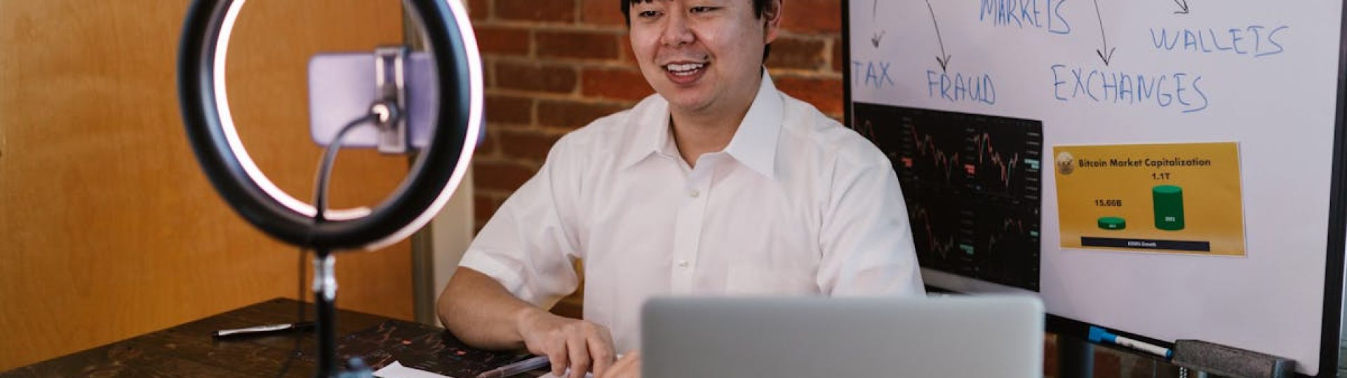 Man discussing cryptocurrency economics with ring light and laptop, engaging content creation.