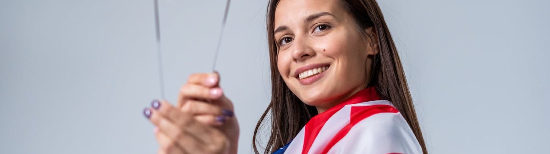 Young woman celebrating Independence Day with sparklers, wrapped in American flag.