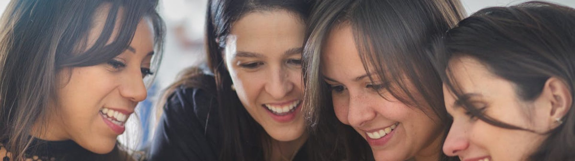 Four women smiling and looking at a smartphone together, creating a warm and joyful atmosphere.