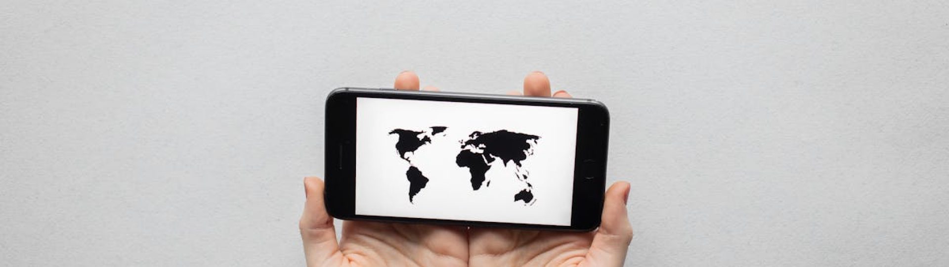 Hands holding a smartphone displaying a world map on a white background.