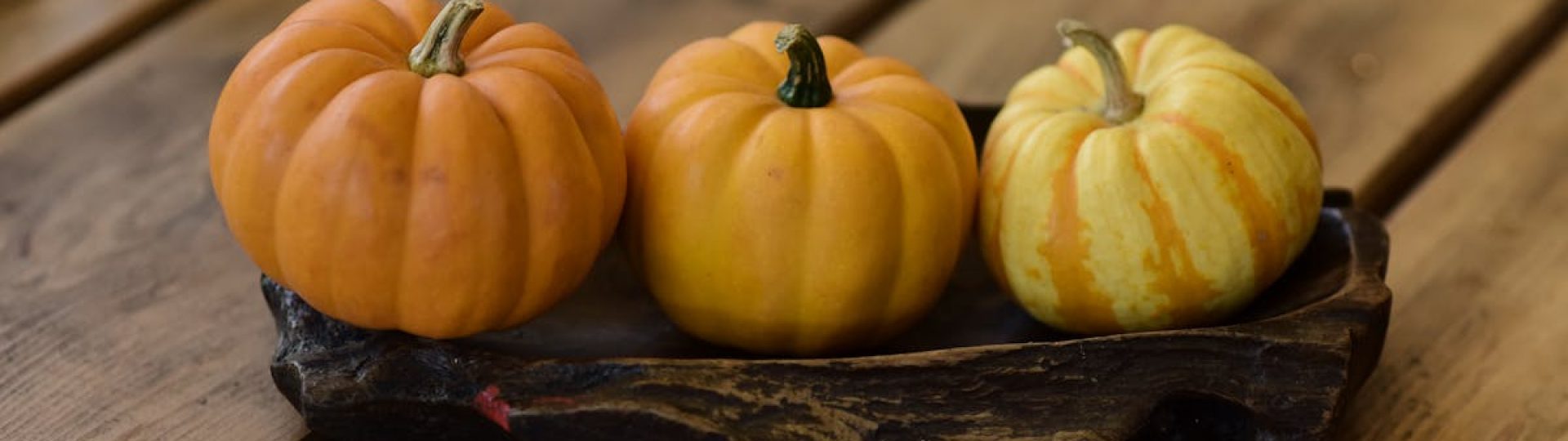 Three mini pumpkins on a wooden tray create a cozy autumn scene.