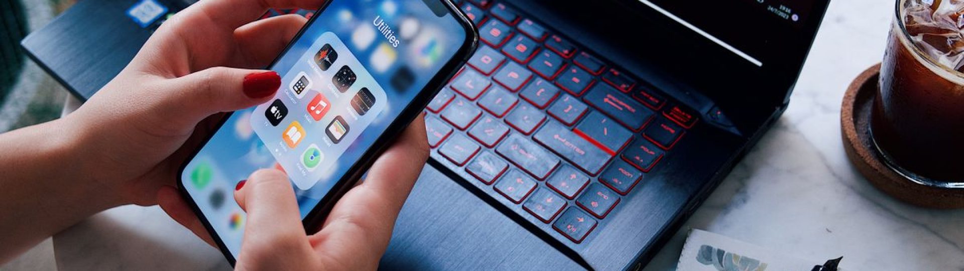 Hands holding a smartphone over a laptop with iced drink. Modern technology in everyday life.
