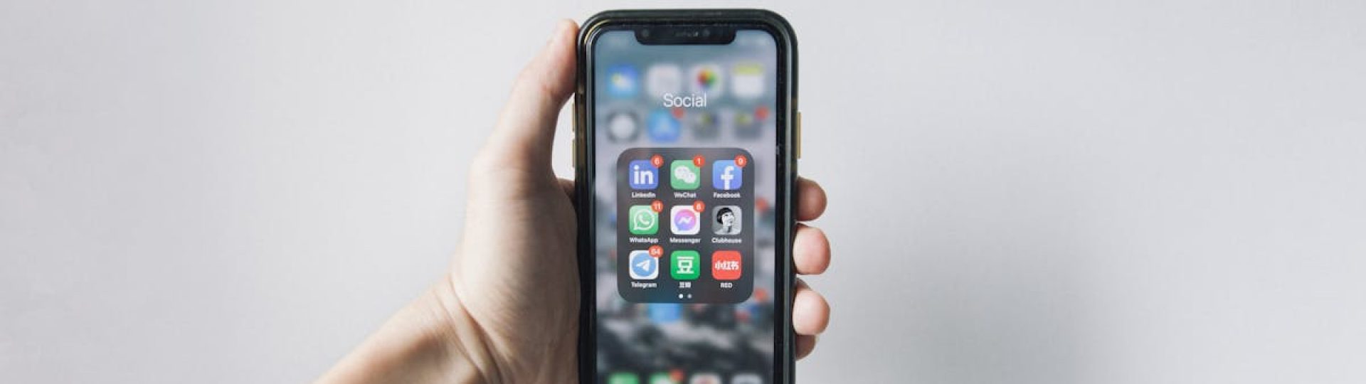 Hand holding smartphone displaying social media apps on home screen.