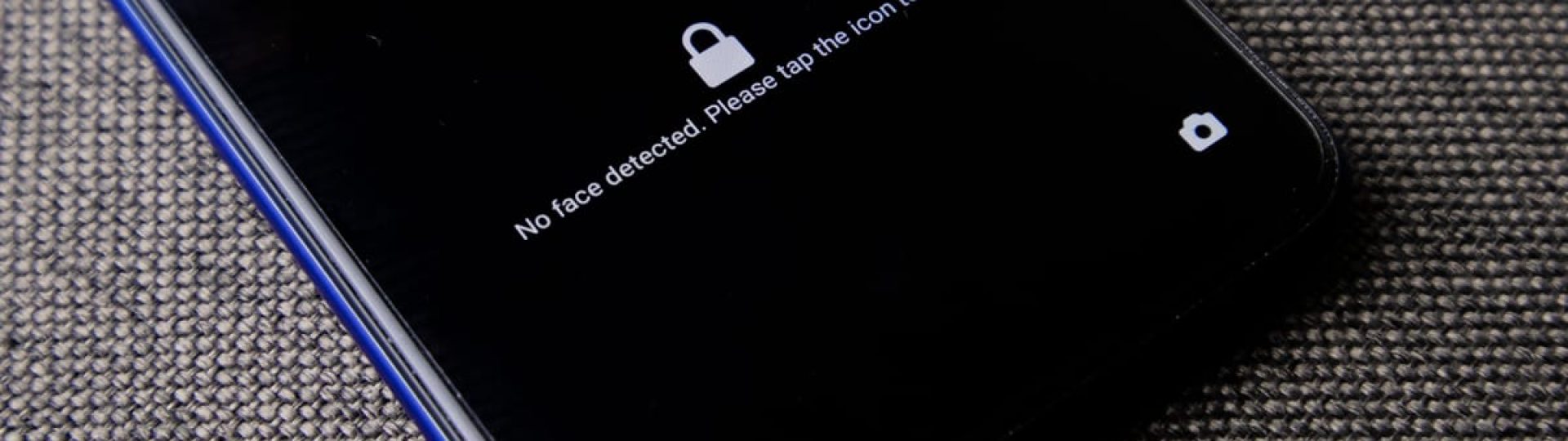 Mobile phone with no face detected message on lock screen on a textured fabric surface.