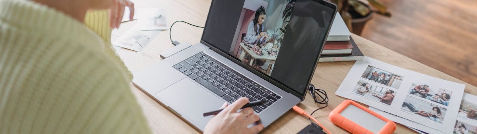 Side view of crop anonymous female editing photos on netbook while sitting at table with graphic tablet in room with potted plants
