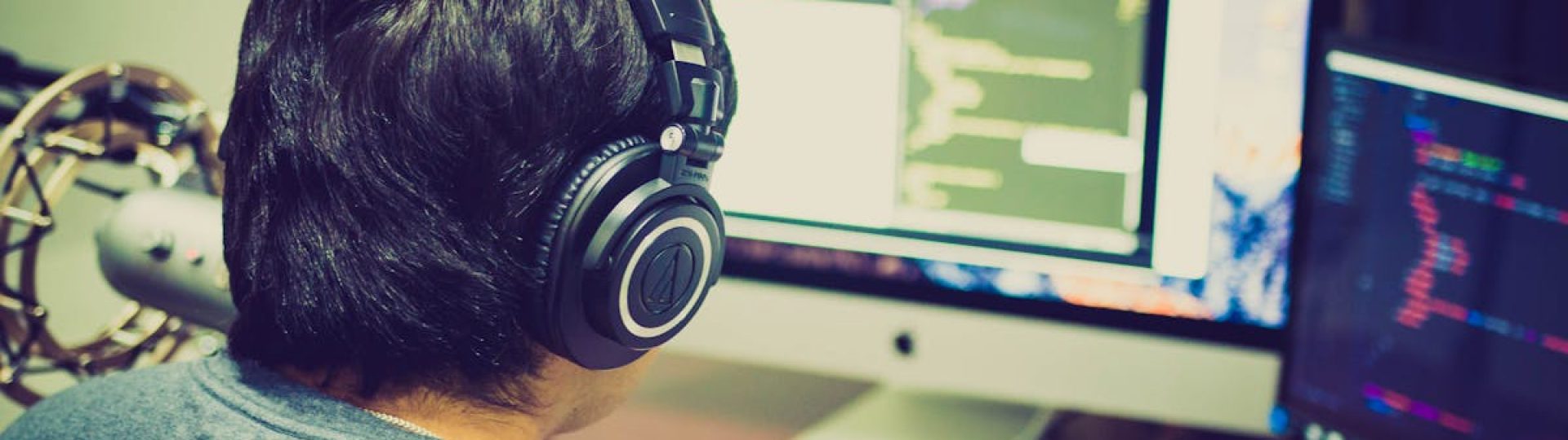 A programmer with headphones focuses on coding at a computer setup with dual monitors.