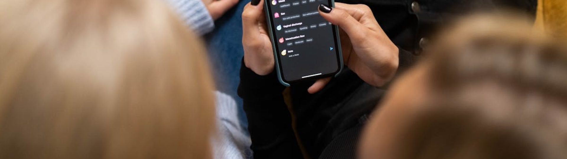 Two women browsing social media together on a smartphone indoors.