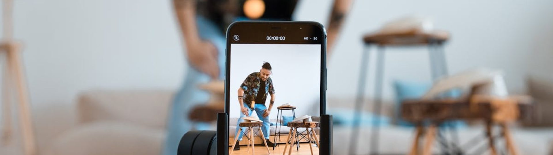 Man recording video content with smartphone on a tripod in a cozy living room.
