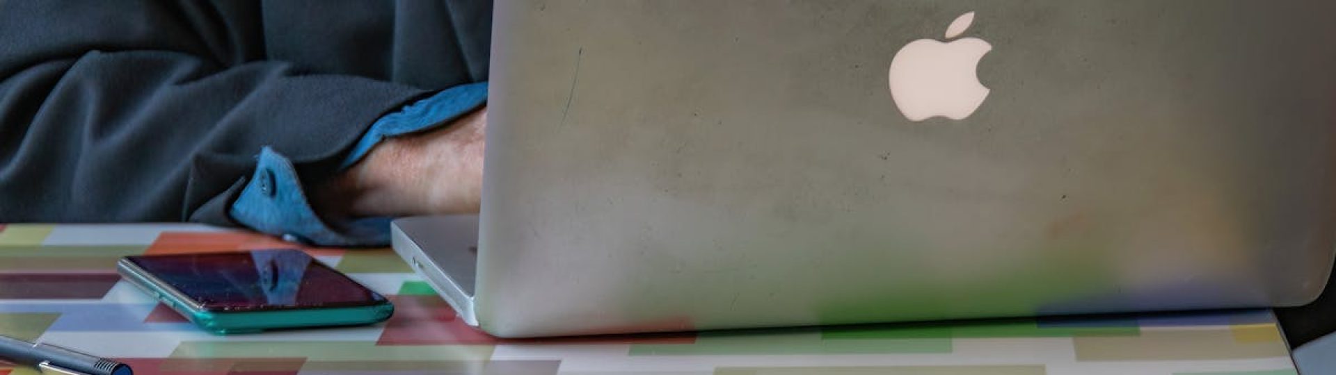 Close-up of a person using a laptop and smartphone on a colorful patterned table indoors.