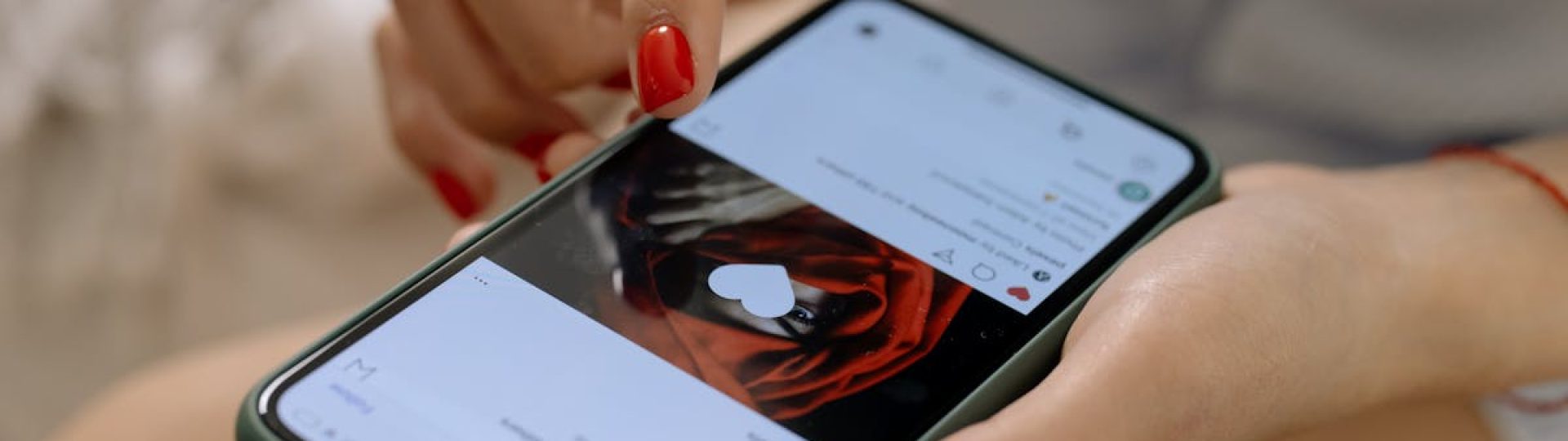 Close-up of a woman with red nails using a smartphone indoors, showcasing social media browsing.
