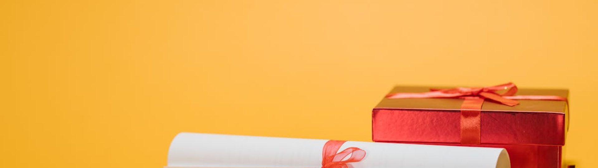 A red gift box and diploma with ribbons on a vibrant yellow background symbolizing celebration and achievement.