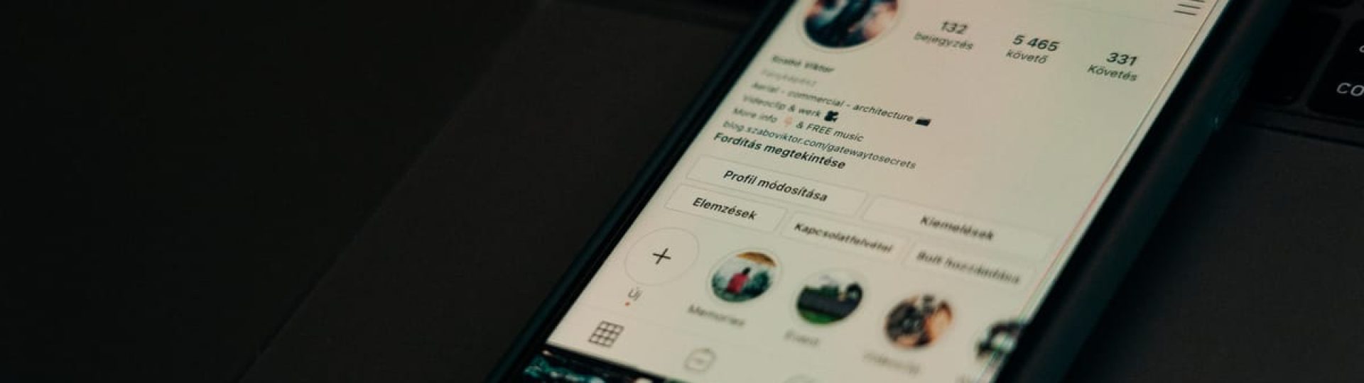 Close-up of smartphone showing a social media profile screen next to a laptop.