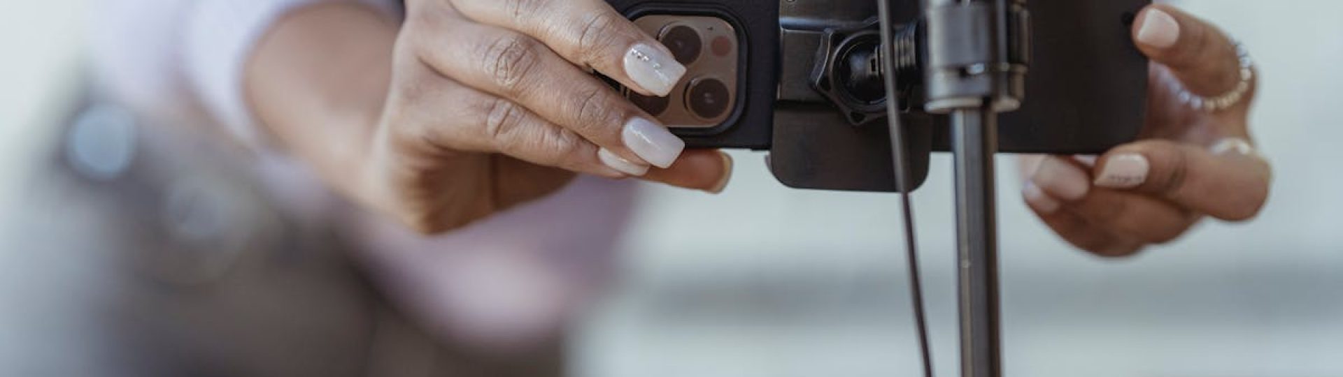 Crop unrecognizable female setting mobile phone on tripod while recording vlog on blurred background