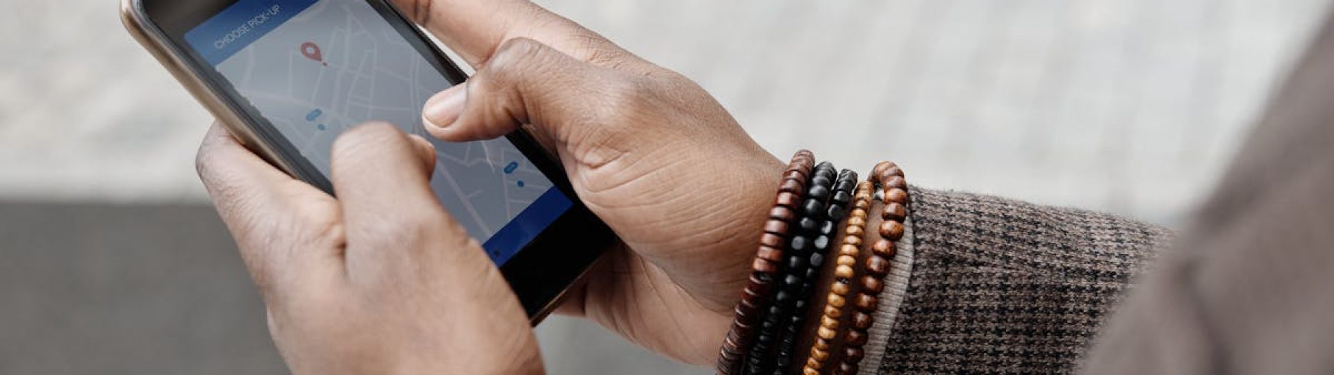 Close-up of hands with bracelets navigating on smartphone using GPS app outdoors.