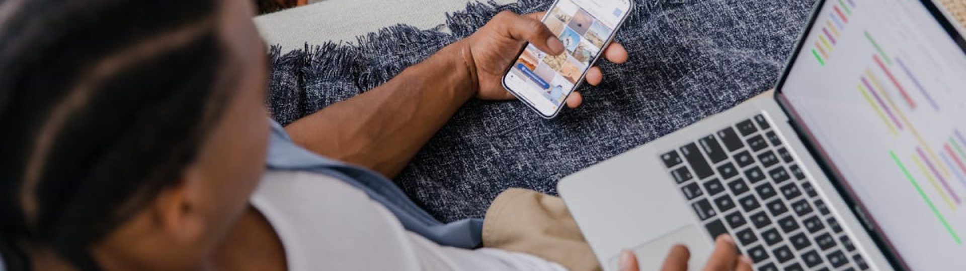 Man multitasking with a smartphone and laptop while sitting on a sofa indoors, top view.