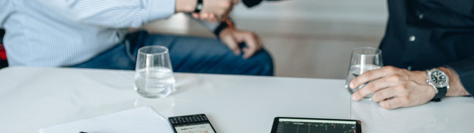 Business meeting with handshake and financial analysis displayed on a tablet.