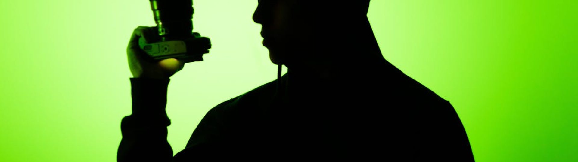 Silhouette of a person holding a camera against a vibrant green background, creating a dramatic effect.