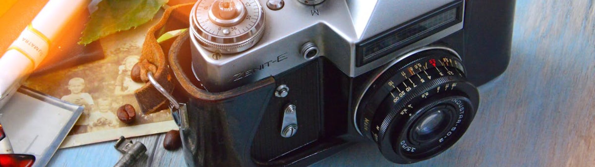 A classic film camera surrounded by nostalgic elements like keys, photos, and roasted coffee beans on a wooden table.