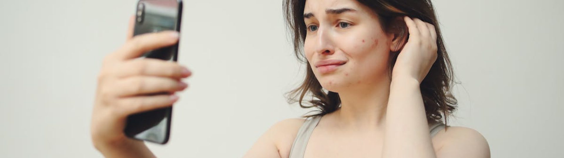 A young woman in a tank top taking a selfie with a worried expression on her face.