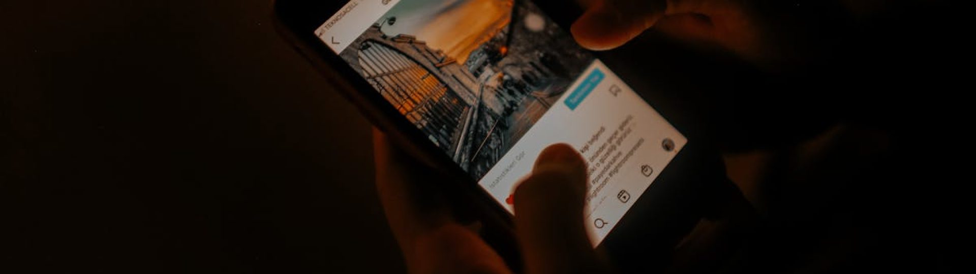 Hands holding a smartphone browsing social media in low light.