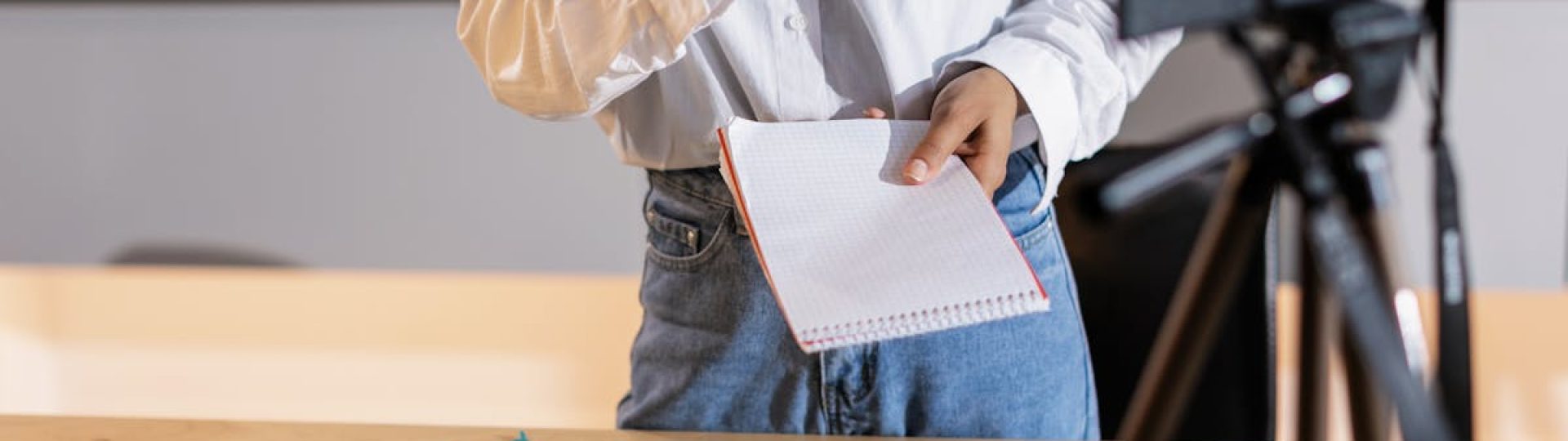 Vlogger recording content with a camera, holding notes and using a laptop in a modern setting.
