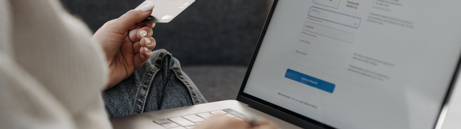 Woman holding credit card shopping online on a laptop from a couch.