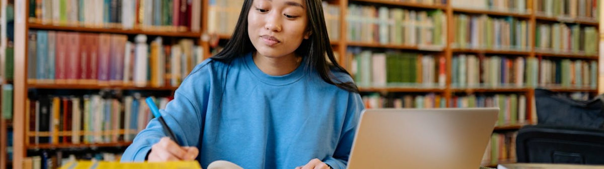 Young woman studying in a library with books and laptop, focusing on education.