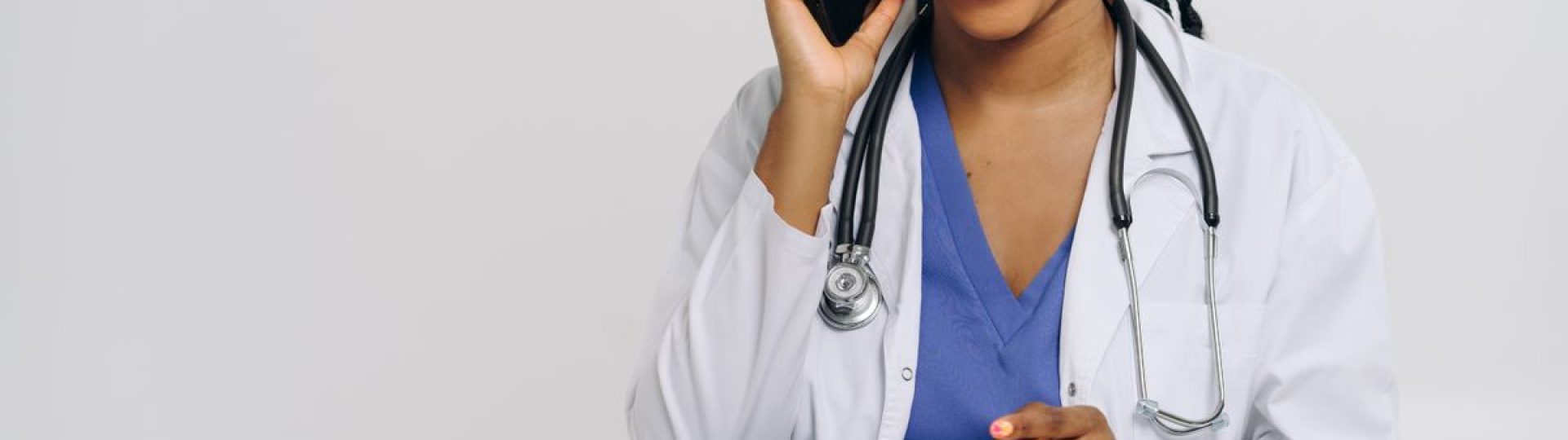 Cheerful female doctor in lab coat talking on smartphone and taking notes.