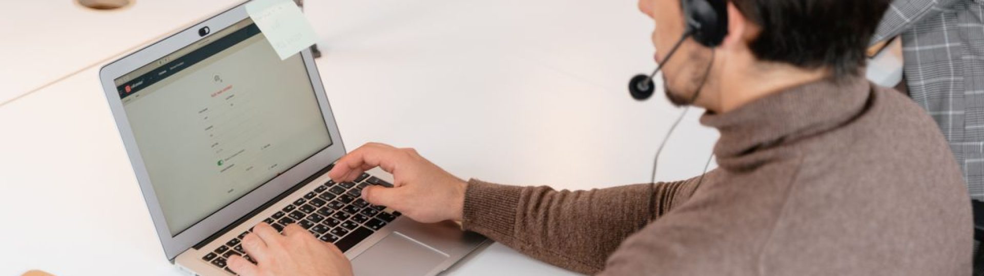 Call center agent wearing headphones working on a laptop in a modern office setting.
