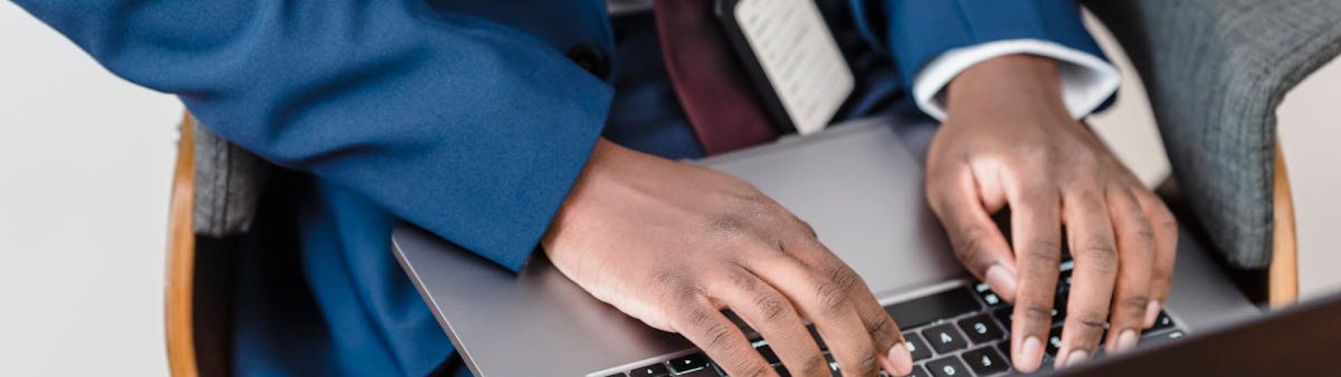 Close-up of a businessman in a blue suit working on a laptop indoors.