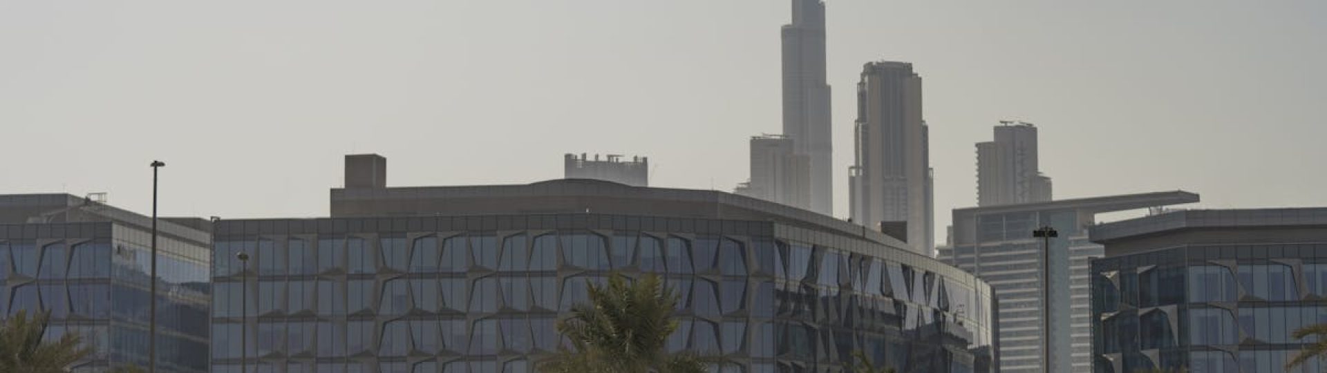 A car parked with a backdrop of Dubai's cityscape and Burj Khalifa under clear skies.